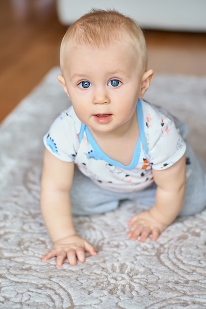 Adorable smiling little boy with big blue eyes is looking, crawling on all fours.