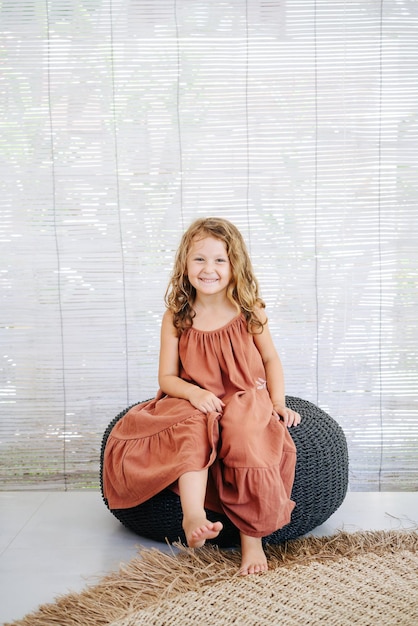 Photo adorable sweet girl 5 years old sits smiling on an ottoman