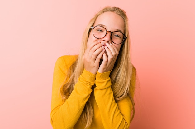 Adorable teenager woman laughing about something, covering mouth with hands.