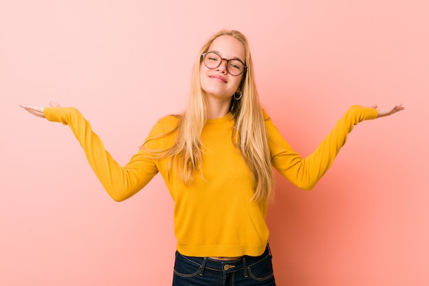 Adorable teenager woman makes scale with arms, feels happy and confident.