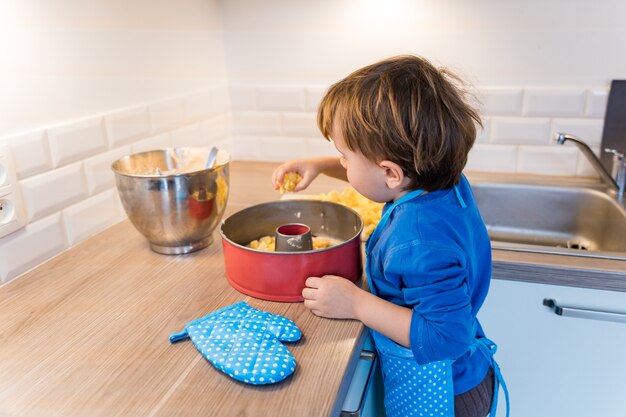 リンゴ国産パイだけを焼くキッチンエプロンを身に着けている愛らしい幼児の男の子