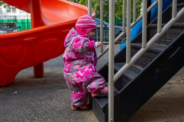 愛らしい幼児が遊び場の階段を登ります。スノースーツを着た幼児の赤ちゃん。秋または冬、寒い季節