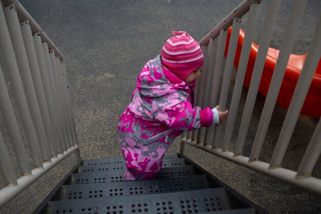 adorable toddler climbs the stairs on the playground. toddler baby dressed in a snowsuit. autumn or winter, cold season