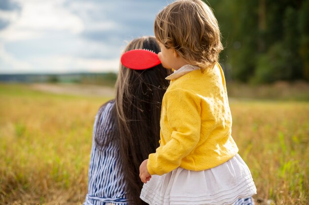 Foto adorabile bambina che pettina i capelli di sua madre all'aperto in una giornata di sole. concetto di amore di madre e figlia