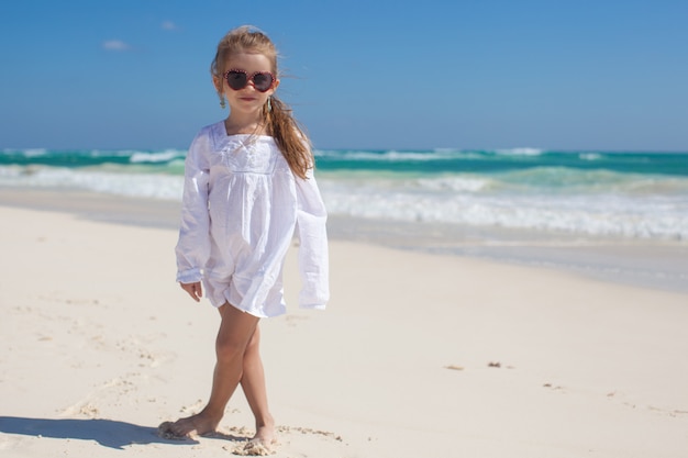 Adorable toddler girl in white dress walking at exotic beach