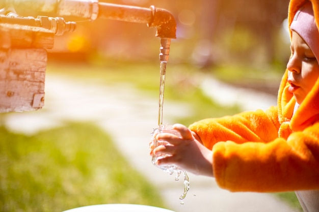 adorable toddler plays with water and tap in the sunshine