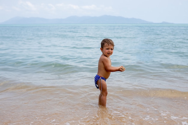 adorable toddler toddler has fun playing on sandy beach of tropical sea.