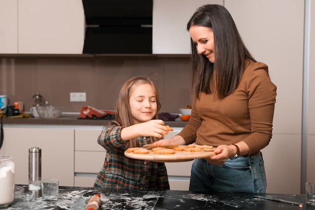 Adorabili due ragazze, una madre e sua figlia stanno preparando dei biscotti natalizi insieme in cucina
