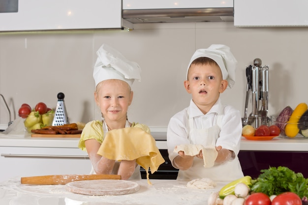 キッチンで軽食を作るシェフの服装の愛らしい白人の子供たち。