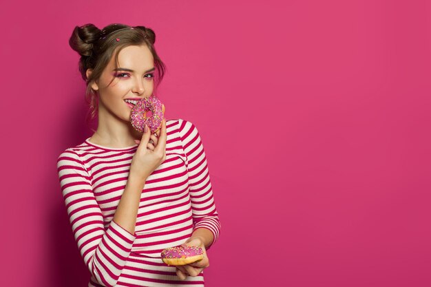 Photo adorable woman eating donut on vibrant pink background fashion portrait