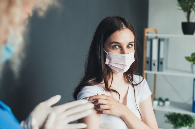 Adorable woman is looking at camera while taking the corona virus vaccine wearing a mask at the hosp...