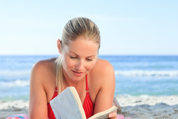 Donna adorabile che legge un libro sulla spiaggia