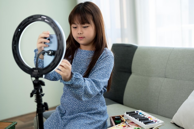 An adorable young Asian girl recording her video or live streaming while painting