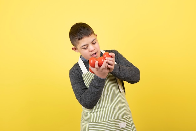 フレッシュトマトを見ているエプロンのダウン症の愛らしい少年。