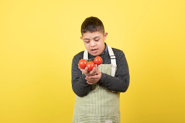 Adorable young boy with down syndrome in apron looking at fresh tomatoes.