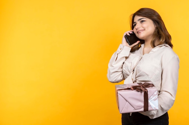 Adorable young girl holding present box and talking on the phoneYoung girl on yellow background High quality photo