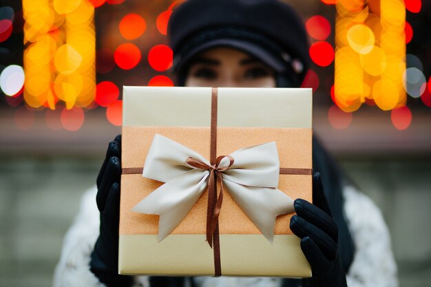 Adorable young model wearing fur coat and cap pulls a gift box to you