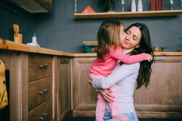 adorable young mother hugs her little funny daughter in kitchen. happy family indoor lifestyle portrait.