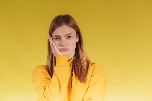 Adorable young teen girl wearing a yellow hoodie Posing for a photographer on a yellow background The teenager is worried