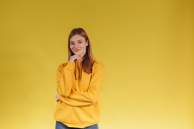 Adorable young teen girl wearing a yellow hoodie Posing for a photographer on a yellow background