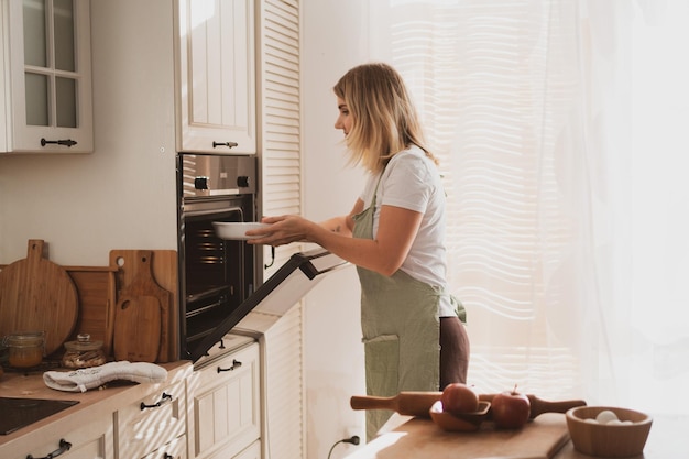 Adorable young woman in chef's apron puts apple pie in the oven