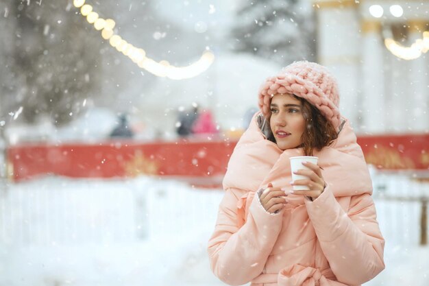 愛らしい若い女性は、花輪を背景にホリデーフェアで歩くニット帽をかぶっています。空きスペース