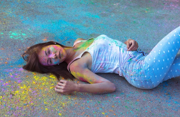 Adorable young woman with short hair covered Holi powder, lying on the asphalt