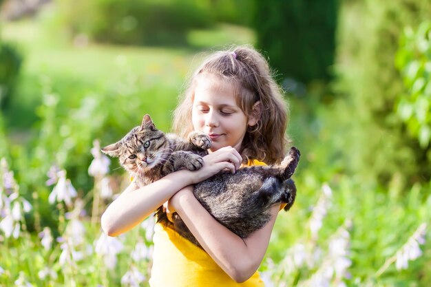 Девушка adorale в желтом платье, держа в руках симпатичного кота. ребенок и домашнее животное на открытом воздухе в летний день.