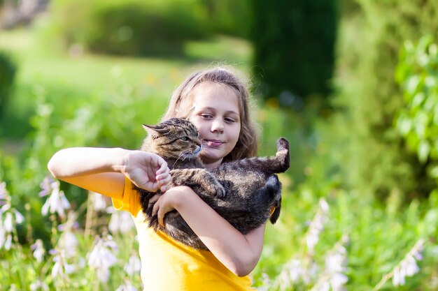 Adorale girl in yellow dress holding lovely cat in her hands. Child and pet outdoors in summer day.