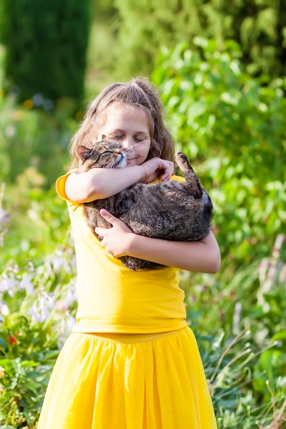 Photo adorale girl in yellow dress holding lovely cat in her hands. child and pet outdoors in summer day.