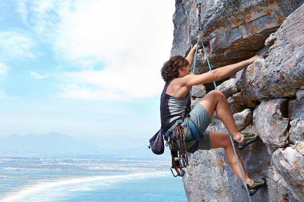 Adrenaline is pushing her to the summit A young woman climbing up a rock face while framed against a blue sky