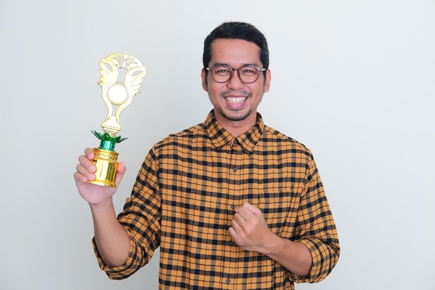 Photo adult asian man clenched fist showing happiness when holding trophy