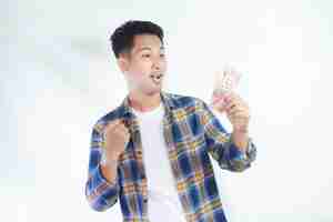 Photo adult asian man clenched fist while holding indonesia paper money and showing excited expression