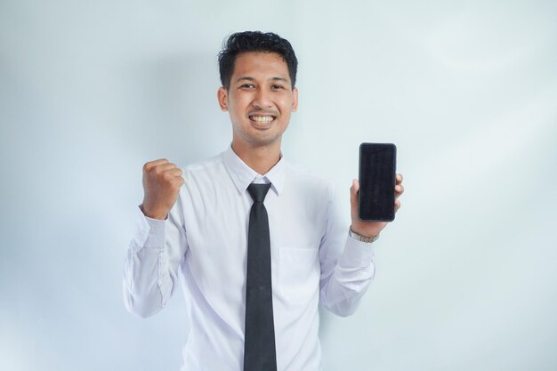 Photo adult asian man clenched fist with excited expression while showing blank mobile phone screen