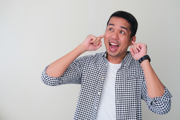 Adult Asian man cover his ears with finger and showing excited face expression