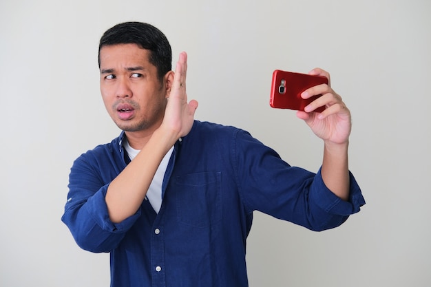 Photo adult asian man cover his face with hand to keep away from his mobile phone