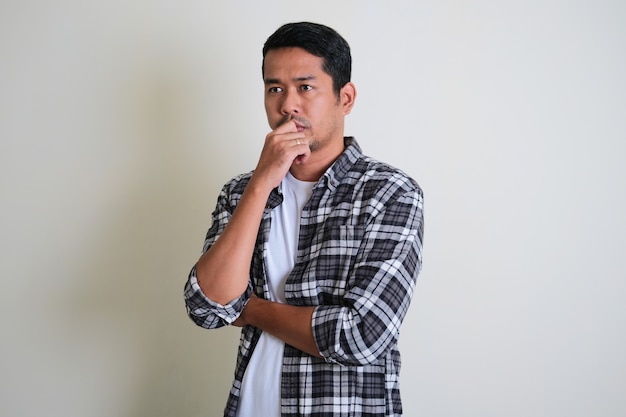 Adult Asian man doing thinking gesture while looking far ahead