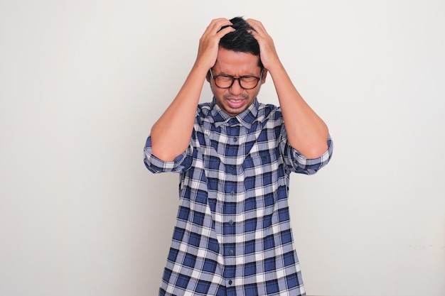 Foto uomo adulto asiatico rivolto verso il basso con le mani che gli afferrano i capelli mostrando un'espressione di stress