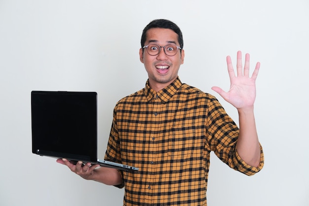 Adult Asian man holding a laptop while give five fingers sign with happy expression