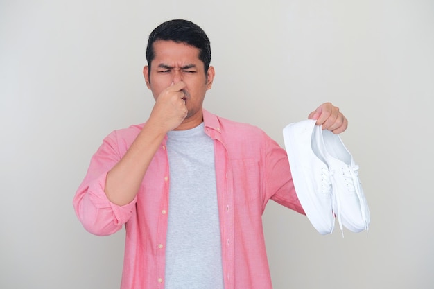Adult Asian man holding smelly white shoes while closed his nose