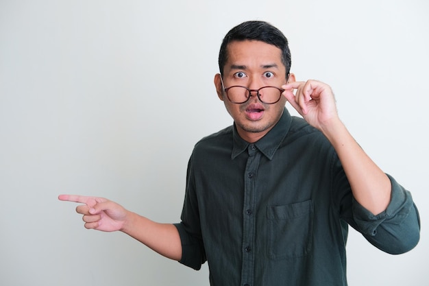 Adult Asian man looking camera with shocked expression while pointing to the right side