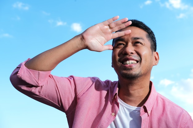 Adult Asian man looking far ahead with happy face expression on bright blue sky background