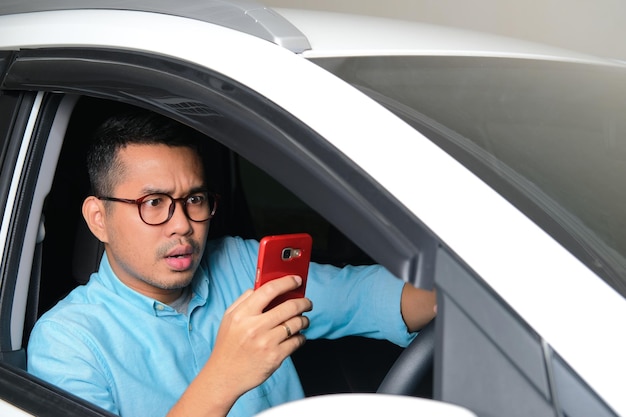 차를 운전하는 동안 진지한 표정으로 휴대폰을 바라보는 성인 아시아 남자
