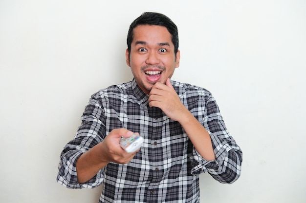 Adult Asian man pointing TV remote forward with excited expression