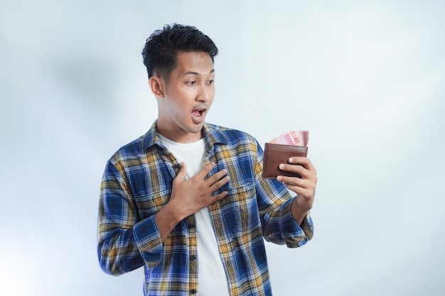 Photo adult asian man showing amazed expression while holding his wallet full of money