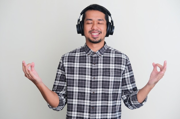 Adult Asian man showing doing meditation pose while enjoying music using headset