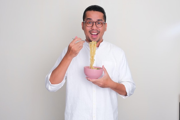 Adult Asian man showing excited expression while eating noodle