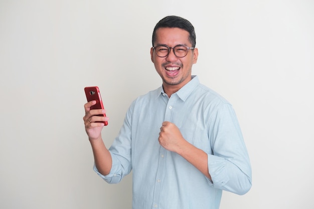 Adult Asian man showing excited expression with fist clenched while holding mobile phone