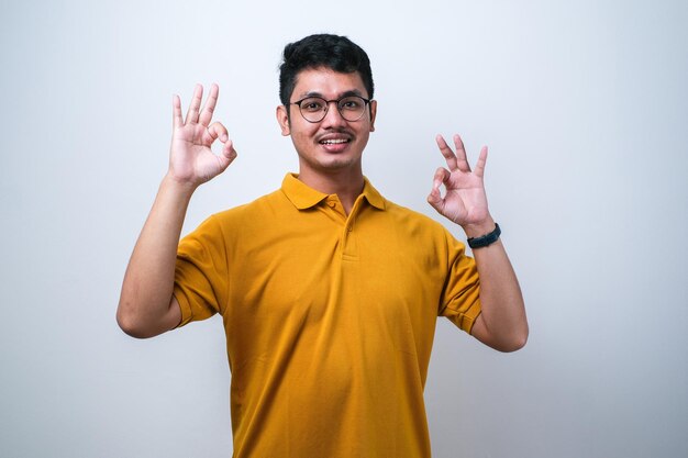 Adult Asian man showing excited face expression while giving two OK finger sign over white background