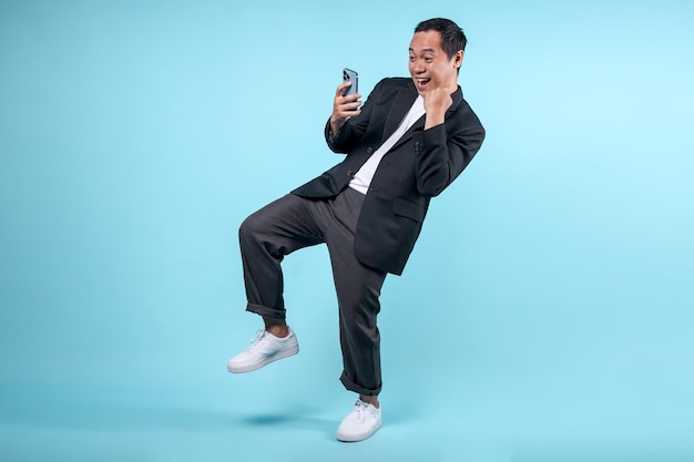 Взрослый азиатский мужчина показывает возбужденный жест, глядя на экран мобильного телефона